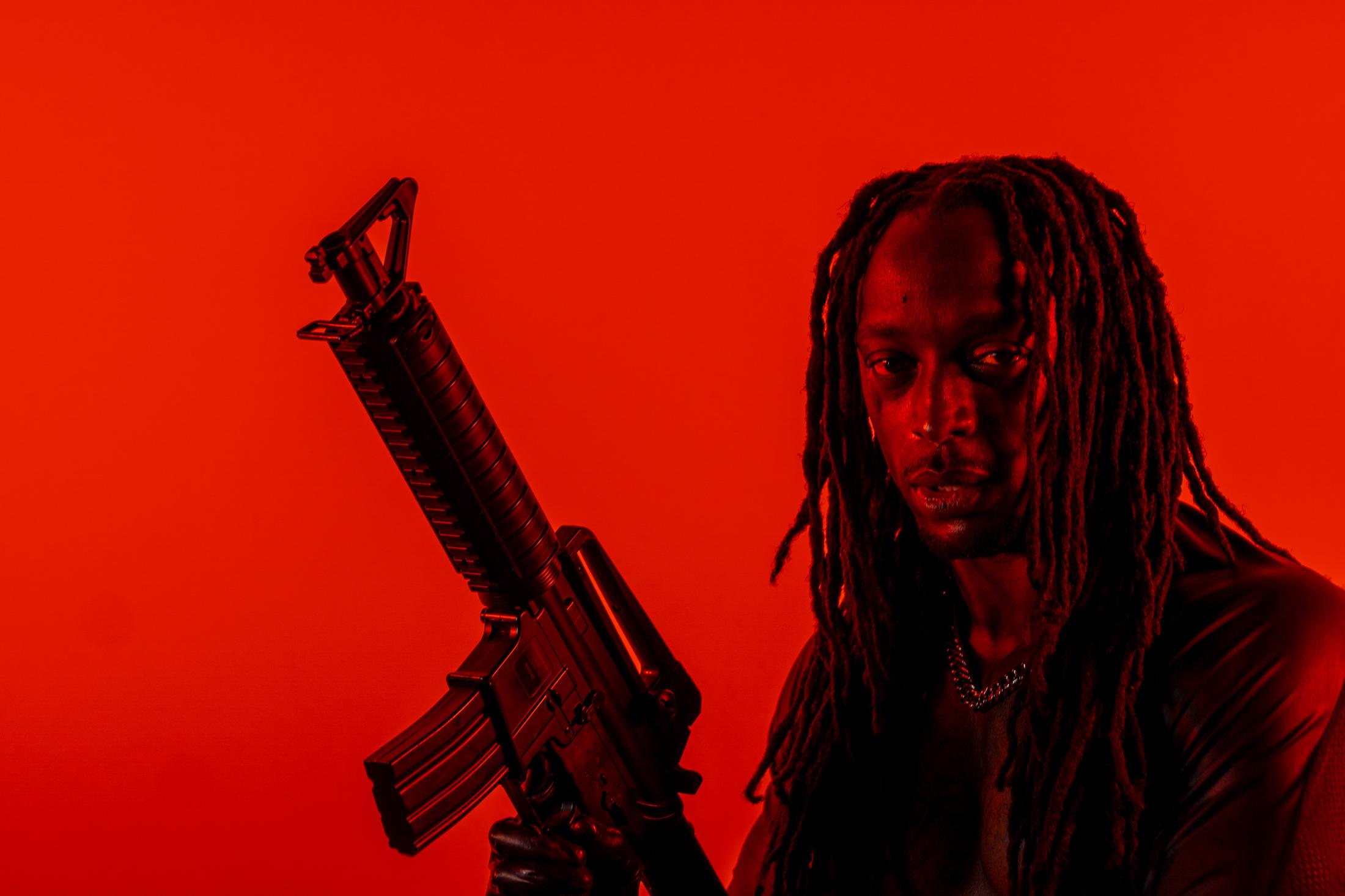 Portrait d’un homme aux dreadlocks tenant un fusil, baigné de lumière rouge