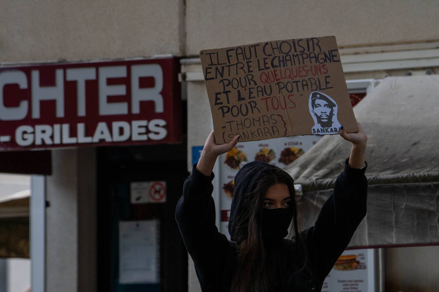 Manifestante masquée brandissant une pancarte devant une vitrine
