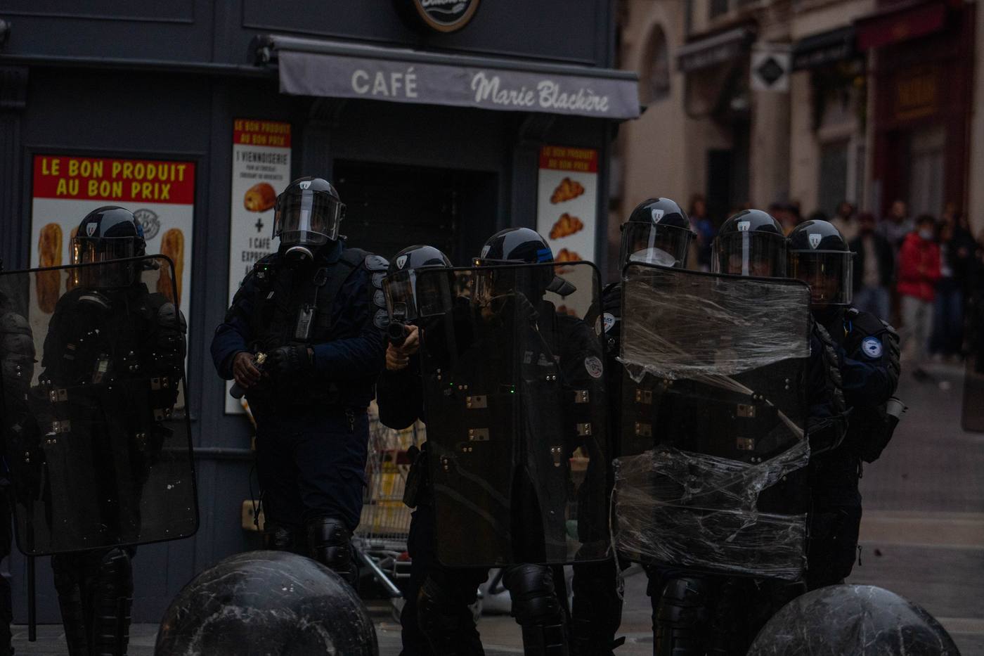 Ligne de policiers casqués avec boucliers devant un café